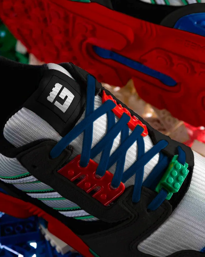 A LEGO Games sneaker: the brick G on its tongue, navy laces running through red and green brick-shaped lace keepers